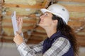 Female builder with clipboard looking at ceiling in development property