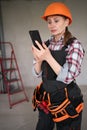 Female builder inside of building in construction or renovation process, typing a message on smartphone, taking a break from Royalty Free Stock Photo