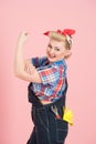 Female builder with red head scurf in blue denim with key in pocket and shows hand off isolated on pastel pink background