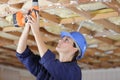 female builder using cordless drill on ceiling joists