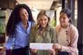 Female Business Team Stand At Desk In Open Plan Office Approving Checking Proofs Or Design Layouts Royalty Free Stock Photo