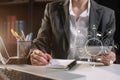 Female businessman hand working at a computer and writing on a notepad with a pen in the office. on the wooden desk there a graph Royalty Free Stock Photo