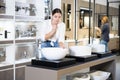 in plumbing department,thoughtful woman inspects round white ceramic sinks with faucets