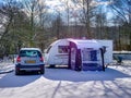 A female caravanner opens a window in a caravan, parked next to a tow car on a sunny winter in winter