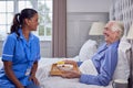 Female Care Worker In Uniform Bringing Senior Man At Home Breakfast In Bed On Tray Royalty Free Stock Photo