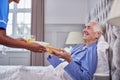 Female Care Worker In Uniform Bringing Senior Man At Home Breakfast In Bed On Tray Royalty Free Stock Photo