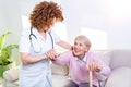 Female caregiver helping senior woman get up from couch in living room. Smiling nurse assisting senior woman to get up. Caring Royalty Free Stock Photo