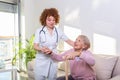 Female caregiver helping senior woman get up from couch in living room. Smiling nurse assisting senior woman to get up. Caring Royalty Free Stock Photo