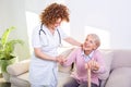 Female caregiver helping senior woman get up from couch in living room. Smiling nurse assisting senior woman to get up. Caring Royalty Free Stock Photo