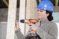 female carpenter using drill on wood house structure