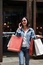Female carrying shopping bags, enjoys talking on the phone while walking at the shopping street Royalty Free Stock Photo