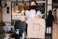 Female cashier with face mask serving coffee to customer, shop open after lockdown. Woman hold packege with food and Royalty Free Stock Photo