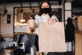Female cashier with face mask serving coffee to customer, shop open after lockdown. Woman hold packege with food and Royalty Free Stock Photo