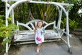 Young caucasian little girl riding on swing in exotic garden, palms in background.