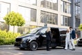 Female chauffeur waits a business people near minivan taxi