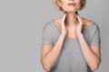 Female checking thyroid gland by herself. Close up of woman in white t- shirt touching neck with red spot. Thyroid