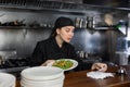 Female chef checks the prepared dish with the paid check in kitchen of the restaurant