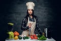 Female chef holds a knife and posing near a table with fresh vegetables. Royalty Free Stock Photo