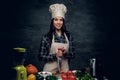 Female chef holds a knife and posing near a table with fresh vegetables. Royalty Free Stock Photo