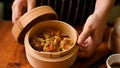 Female chef open a fresh hot bamboo steamer with steamed shrimp dumplings