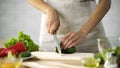 Female chef slicing fresh cucumber with a knife on wooden board, vegetables Royalty Free Stock Photo