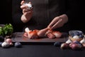 A female chef sprinkles fresh raw chicken drumsticks on a dark background with sea salt. Nearby lie the ingredients for