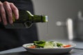 A female chef in a white uniform and a black apron in the restaurant kitchen. Cooking. The cook pours olive oil from a Royalty Free Stock Photo