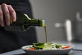 A female chef in a white uniform and a black apron in the restaurant kitchen. Cooking. The cook pours olive oil from a Royalty Free Stock Photo