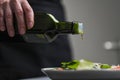 A female chef in a white uniform and a black apron in the restaurant kitchen. Cooking. The cook pours olive oil from a Royalty Free Stock Photo