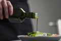 A female chef in a white uniform and a black apron in the restaurant kitchen. Cooking. The cook pours olive oil from a Royalty Free Stock Photo