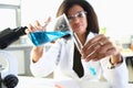 Female chemist pours blue liquid from a flask into test tub Royalty Free Stock Photo