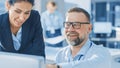 Female Chief Engineer Talks with Electronics Specialist, Explaining Things, He Works on Desktop Co Royalty Free Stock Photo