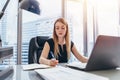 Female chief executive sitting at her desk taking notes in datebook writing with pen and using her computer in modern