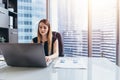 Female chief executive sitting at her desk taking notes in datebook writing with pen and using her computer in modern Royalty Free Stock Photo