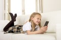 Female child with blond hair lying on home sofa using internet app on mobile phone