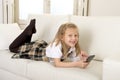 Female child with blond hair lying on home sofa using internet app on mobile phone