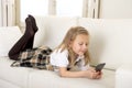 Female child with blond hair lying on home sofa using internet app on mobile phone