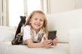 Female child with blond hair sitting on couch using internet app on mobile phone