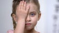 Female child covering eye with hand, ophthalmological exam, nearsightedness