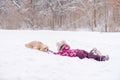 Toddler girl lay in snow and play with dog Royalty Free Stock Photo