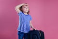 Female child striped blue white t-shirt sitting on a large travel suitcase dream flies rest on the sea shore pink