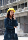 Female civil engineer or architect with yellow helmet, standing and calling with mobile phone and project drafts while in hand Royalty Free Stock Photo