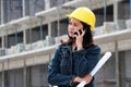 Female civil engineer or architect with yellow helmet, standing and calling with mobile phone and project drafts while in hand Royalty Free Stock Photo