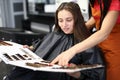 Female client with master in beauty salon examines samples of palette of hair dyes