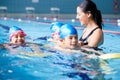 Female Coach In Water Giving Group Of Children Swimming Lesson In Indoor Pool