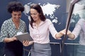 Female Colleagues With Digital Tablet Meeting On Stairs Of Office With World Map In Background