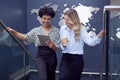 Female Colleagues With Digital Tablet Meeting On Stairs Of Office With World Map In Background