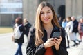 Female college student with phone outdoors. Smiling school girl with backpack standing at campus. Portrait of student outside the