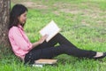 Female college student reading book under the tree in the park Royalty Free Stock Photo