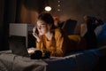 Female college student talking on mobile phone, lying on bed working on laptop at night in dormitory. Royalty Free Stock Photo